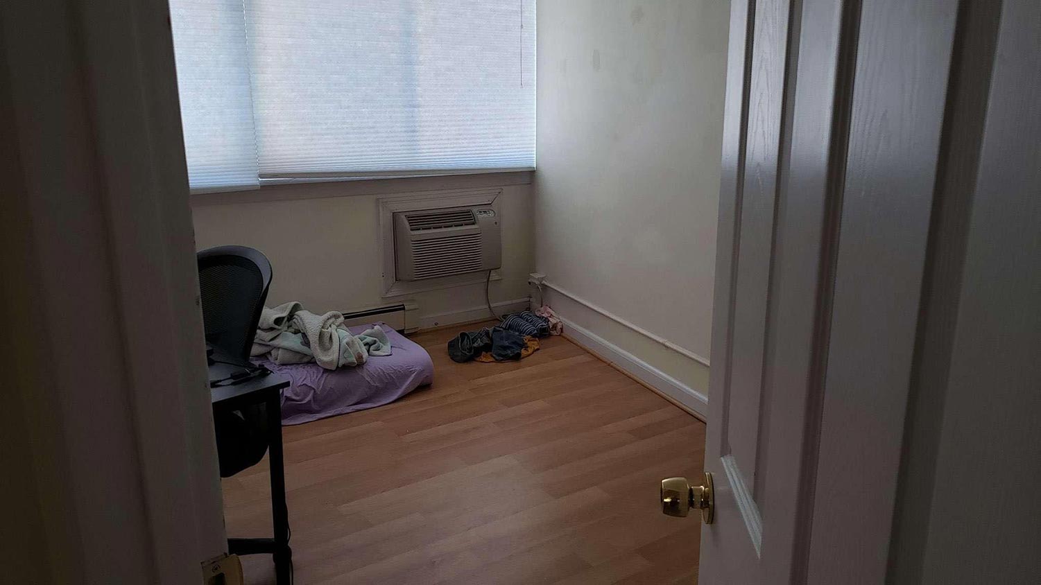 A door to a bedroom opens, only showing a chair and the foam mattress topper folded in half on the floor.